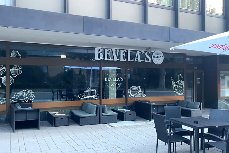 Schaufenster von Bevela's in der Bahnhofstraße mit Schriftzug, Fensterbildern und Sitzplätzen davor