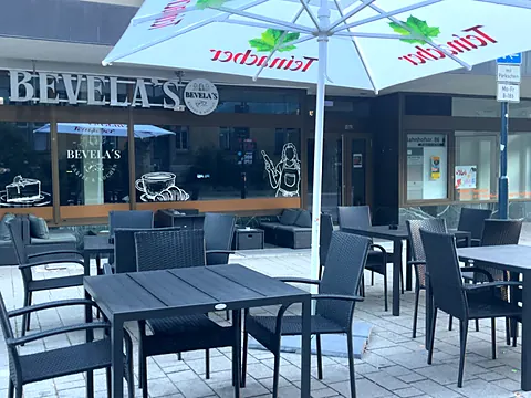 Terrasse vor dem Café mit schwarzen Rattanstühlen, Tischen und Sonnenschirmen