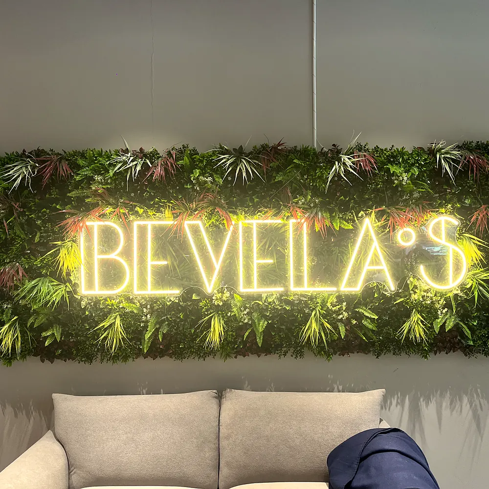 Leuchtender Neon-Schriftzug Bevela's auf einer grünen Pflanzenwand über einer hellen Couch